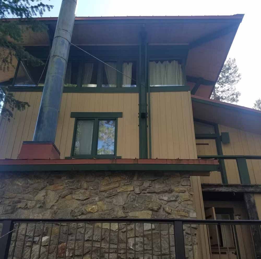 Stone-and-wood house facade with green trim, large overhanging roof, and a metal fence in front.