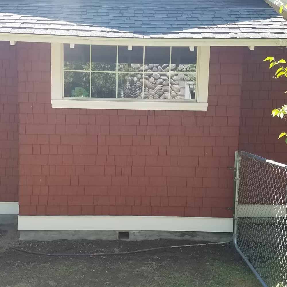 Red shingled house exterior with a white-trimmed window and chain-link fence at right.