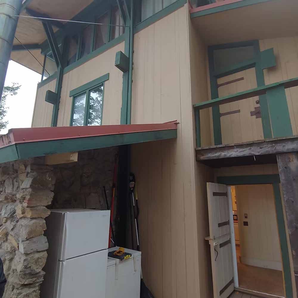 Stone and tan house exterior with green trim, red awning, and open doors under a covered entry