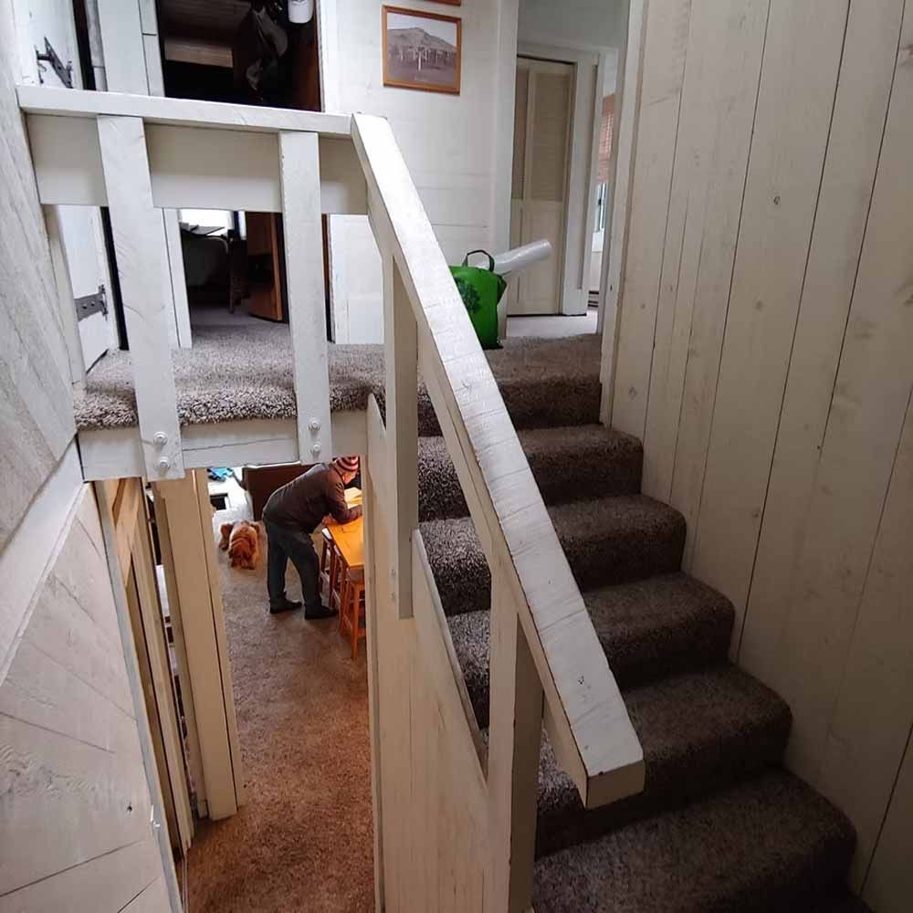 Narrow stairwell with carpeted steps, white railings, and a person working on the lower floor.