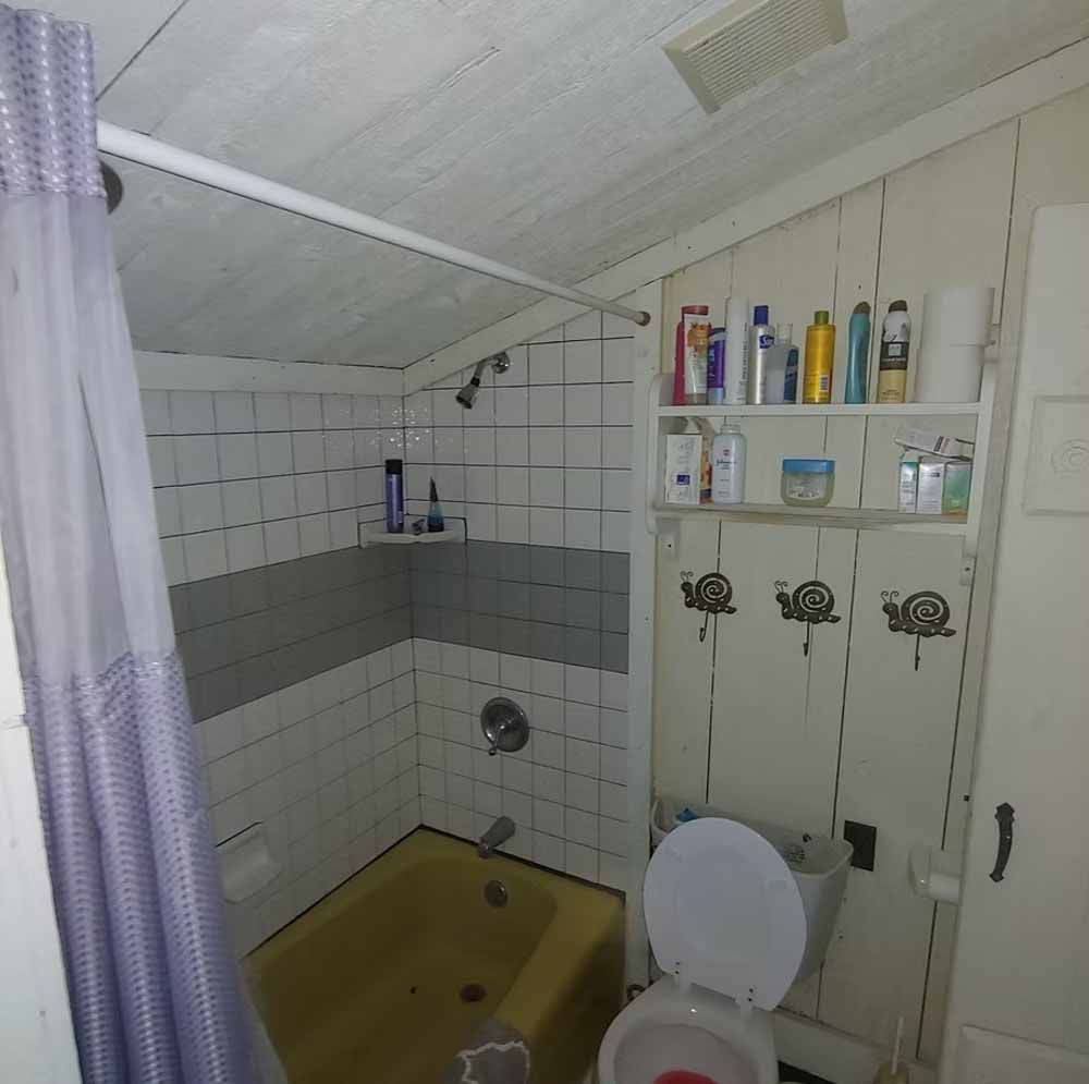 Small bathroom with a yellow tub, white tiled shower, toilet, and wall shelves with toiletries.