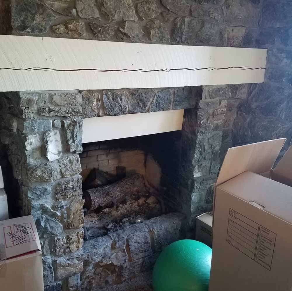 Stone fireplace with white mantel, cardboard box on the right, and a green exercise ball in front.