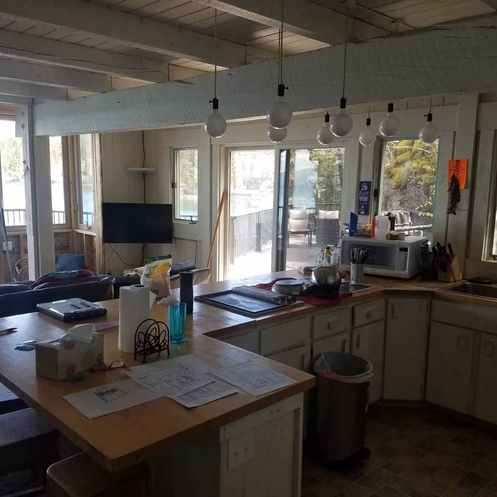 Bright kitchen with island counter, large windows, hanging lights, and microwave on the counter.
