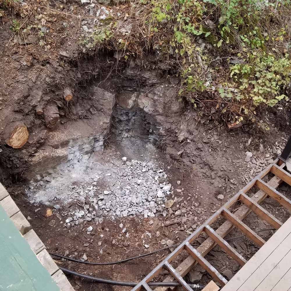 Excavated dirt pit with white gravel at the bottom, beside a wooden ladder on the right.
