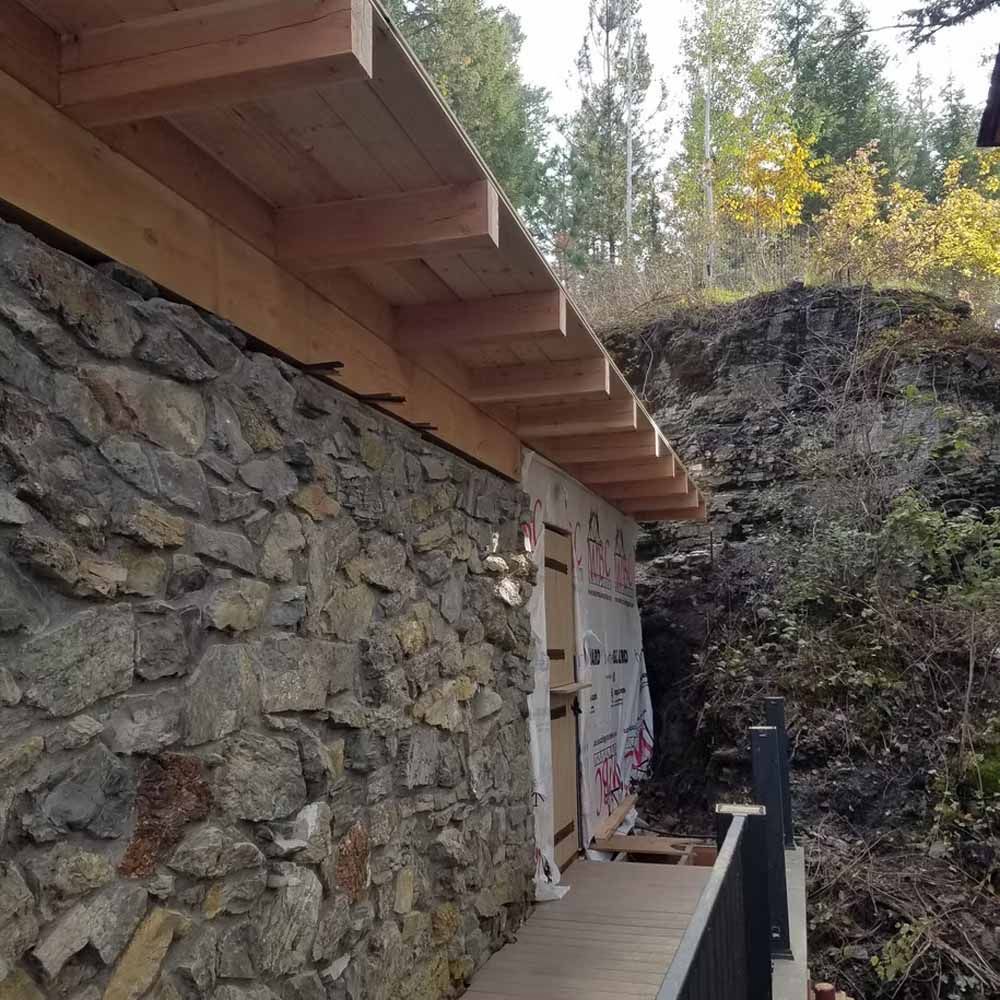 Stone wall with a wooden roof overhang beside a narrow walkway in a wooded hillside setting