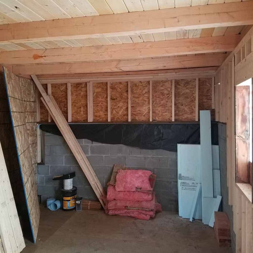 Partially finished shed interior with exposed framing, cinder block walls, and stacked construction materials.