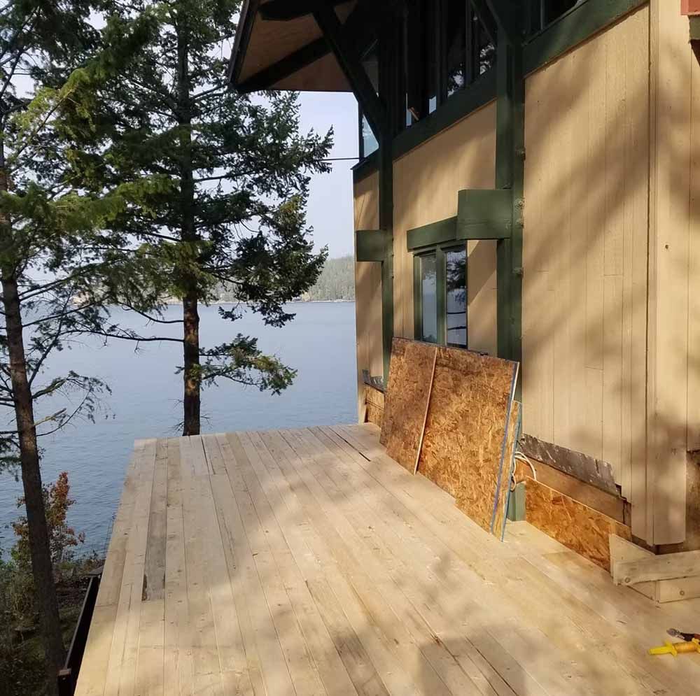 Wooden porch deck beside a cabin, overlooking trees and a hazy body of water