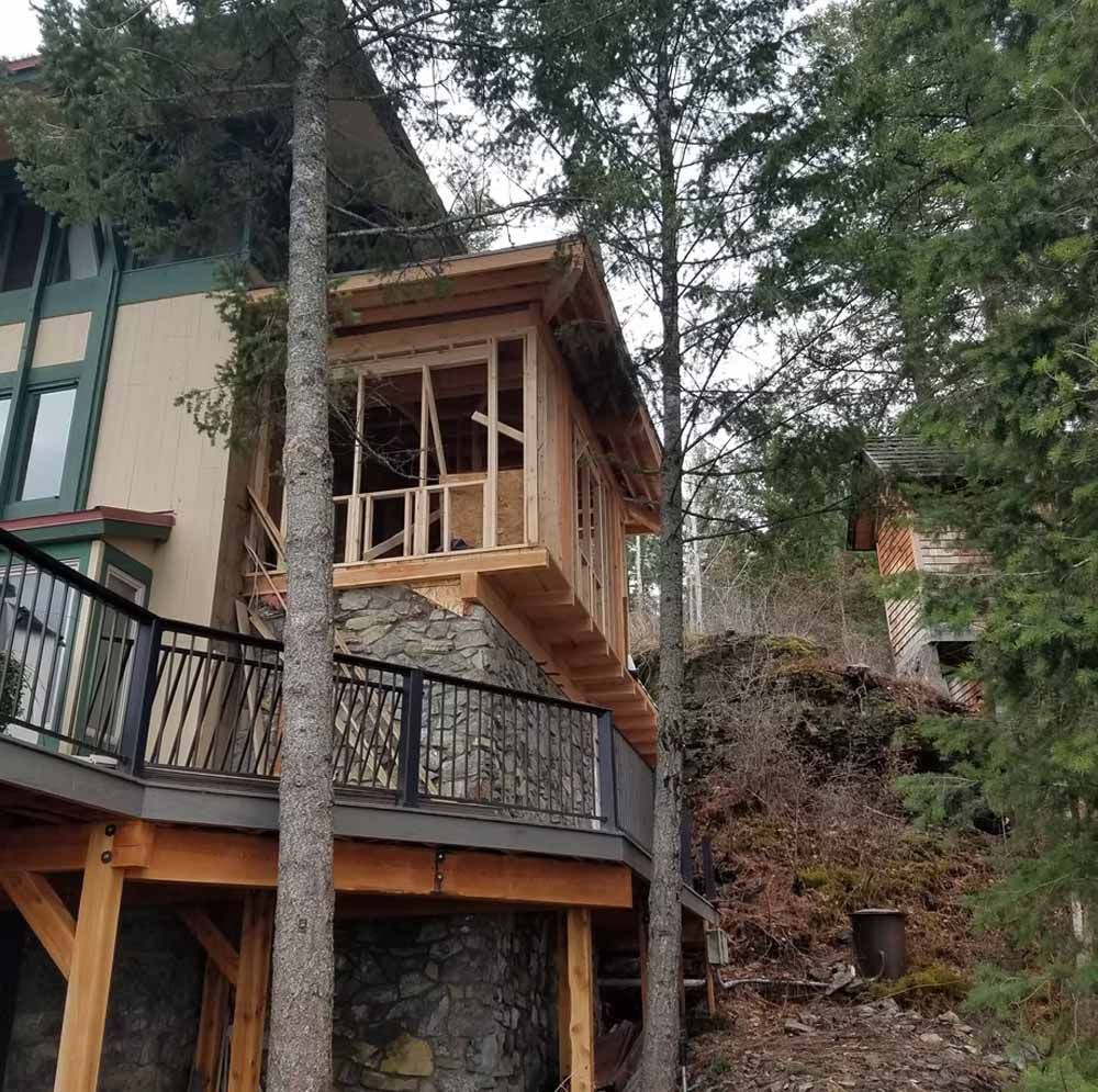 Small wooden balcony addition on a house among tall trees on a wooded hillside