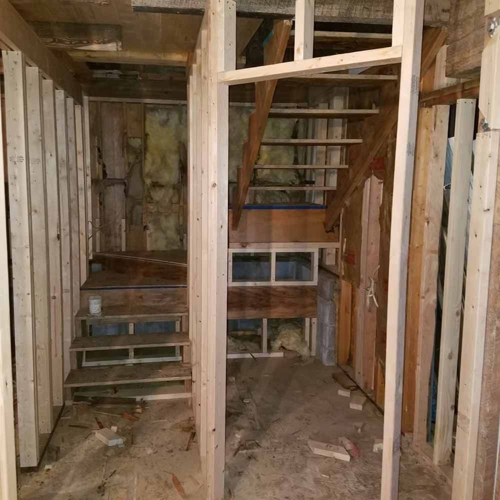 Partially framed unfinished room with exposed wood studs, stairs, and a narrow basement-like corridor