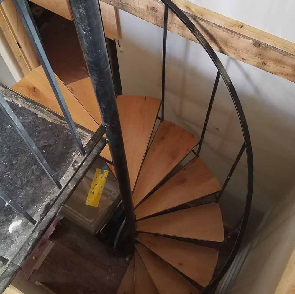 Curved wooden spiral staircase with black metal railing in a narrow interior space