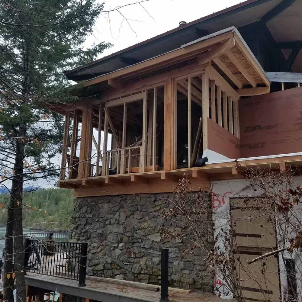 Partially built wooden porch on a stone house with exposed framing and a forested backdrop