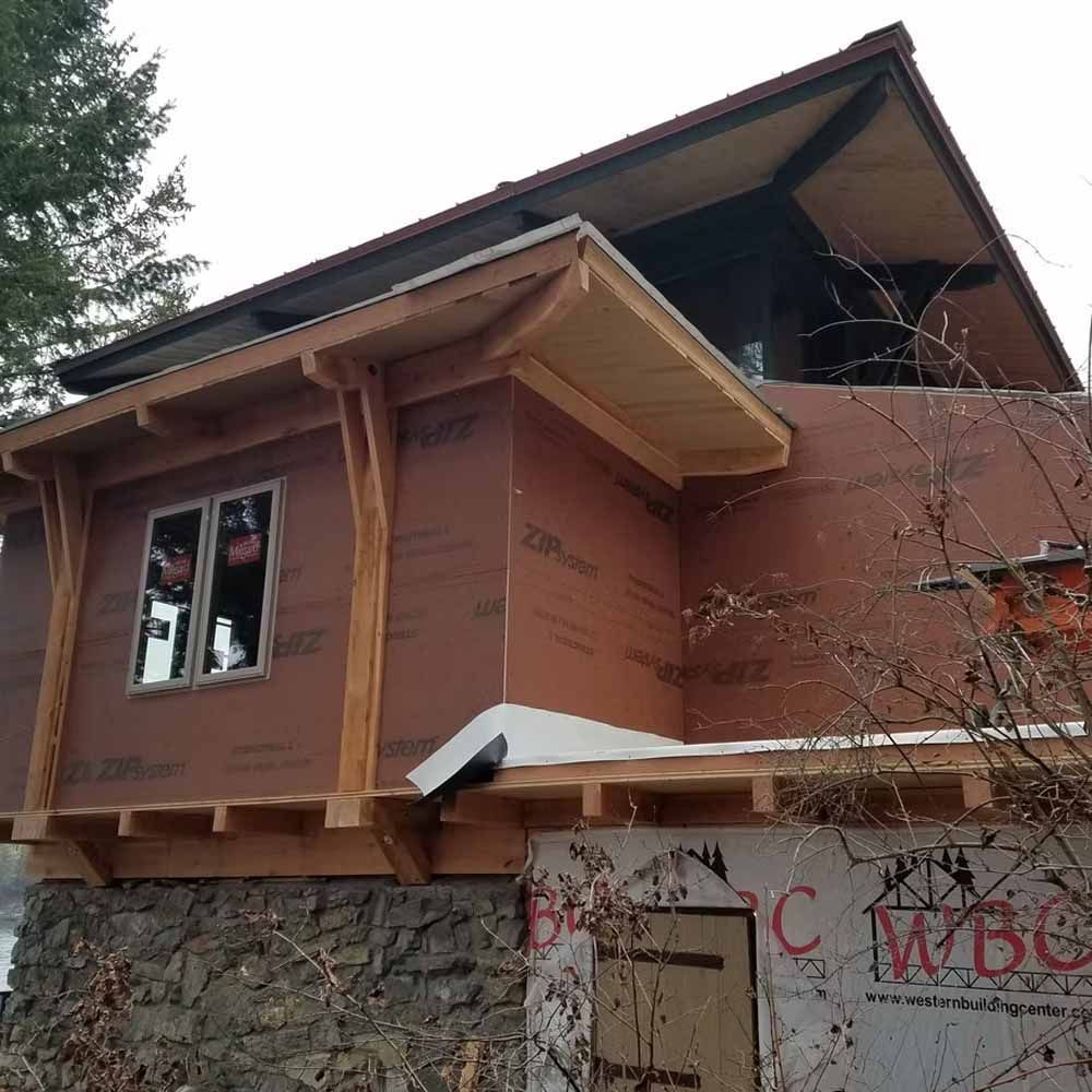 Two-story house under construction with brown sheathing, stone lower wall, and steep roofline
