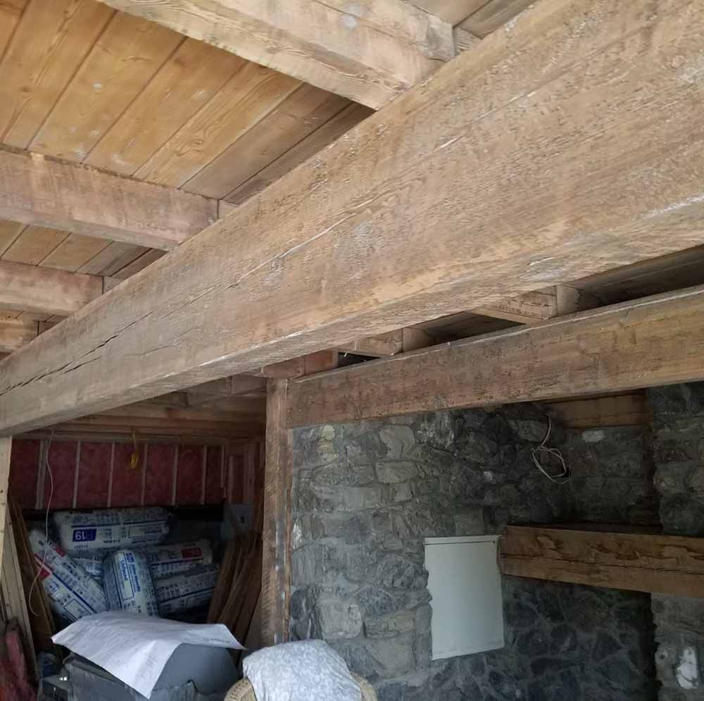 Rustic stone room with exposed wooden beams and stacked supplies in a corner.