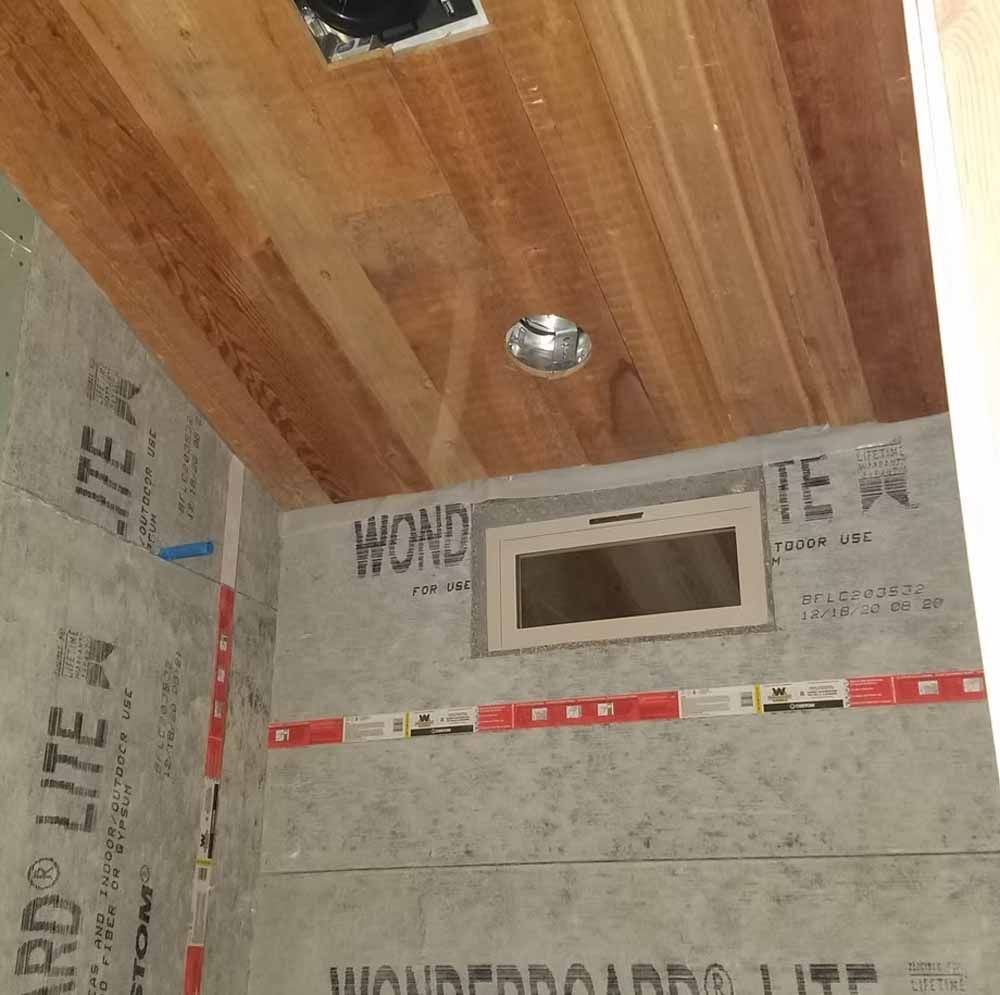 Bathroom under construction with wood ceiling, tiled walls, and a small window opening.