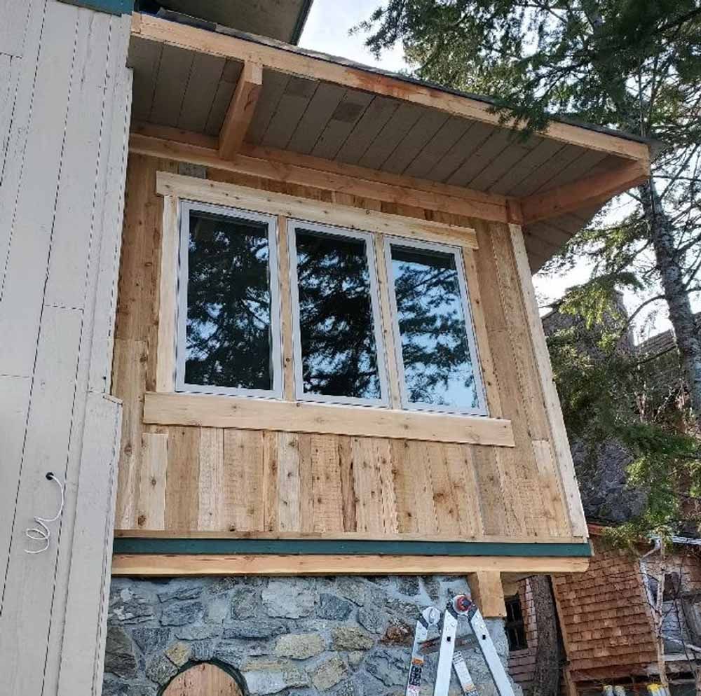 New wood-framed window on a cabin exterior above a stone foundation and ladder