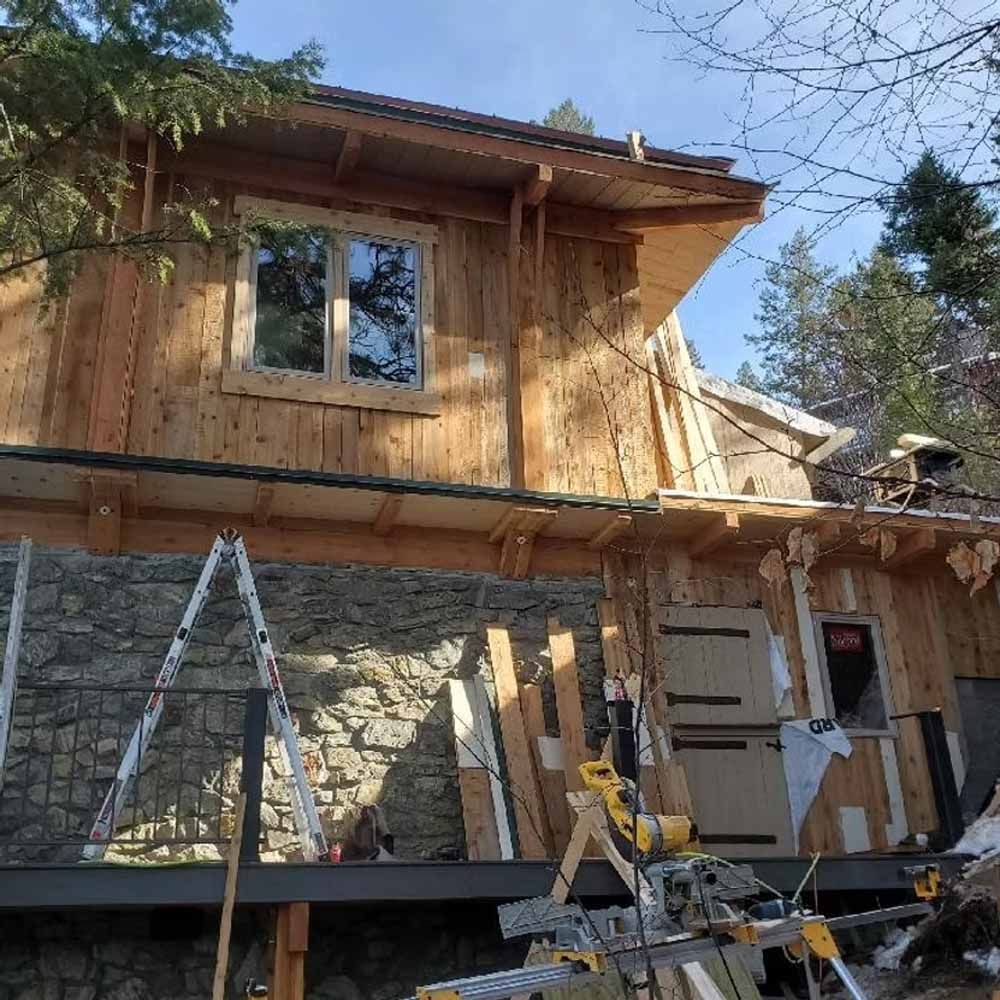 Wood-sided house under construction with ladders, scaffolding, and building materials outside