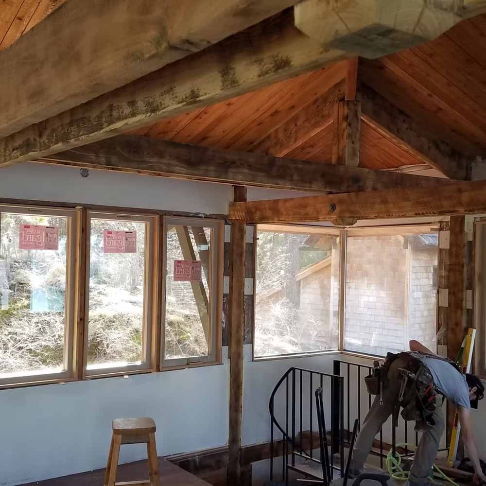 Rustic sunroom with wood beams, windows, a stool, and a spiral staircase under construction