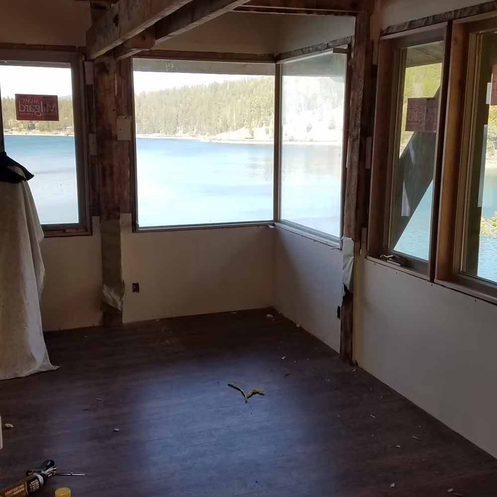 Empty room with large windows overlooking a blue lake and forested shore