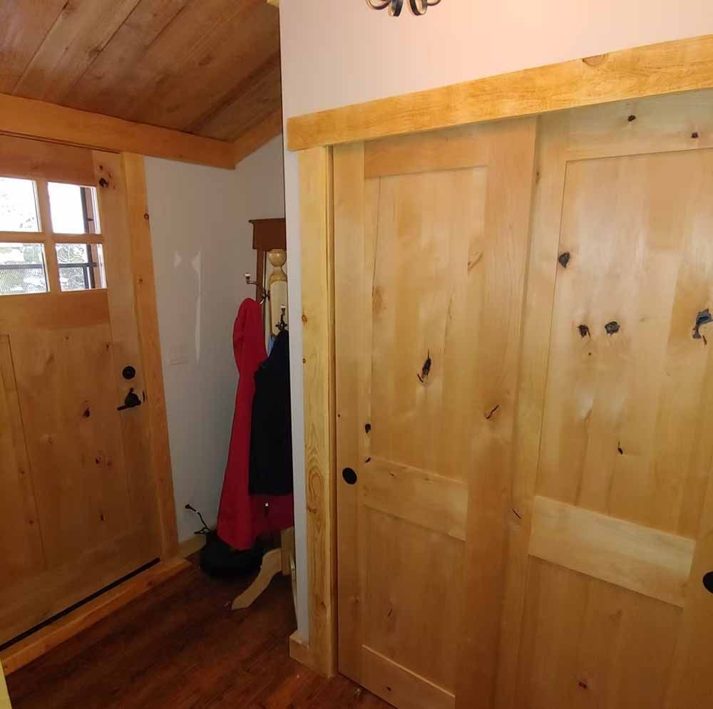 Wooden hallway with large closet doors, entry door, and a red coat hanging on a rack.