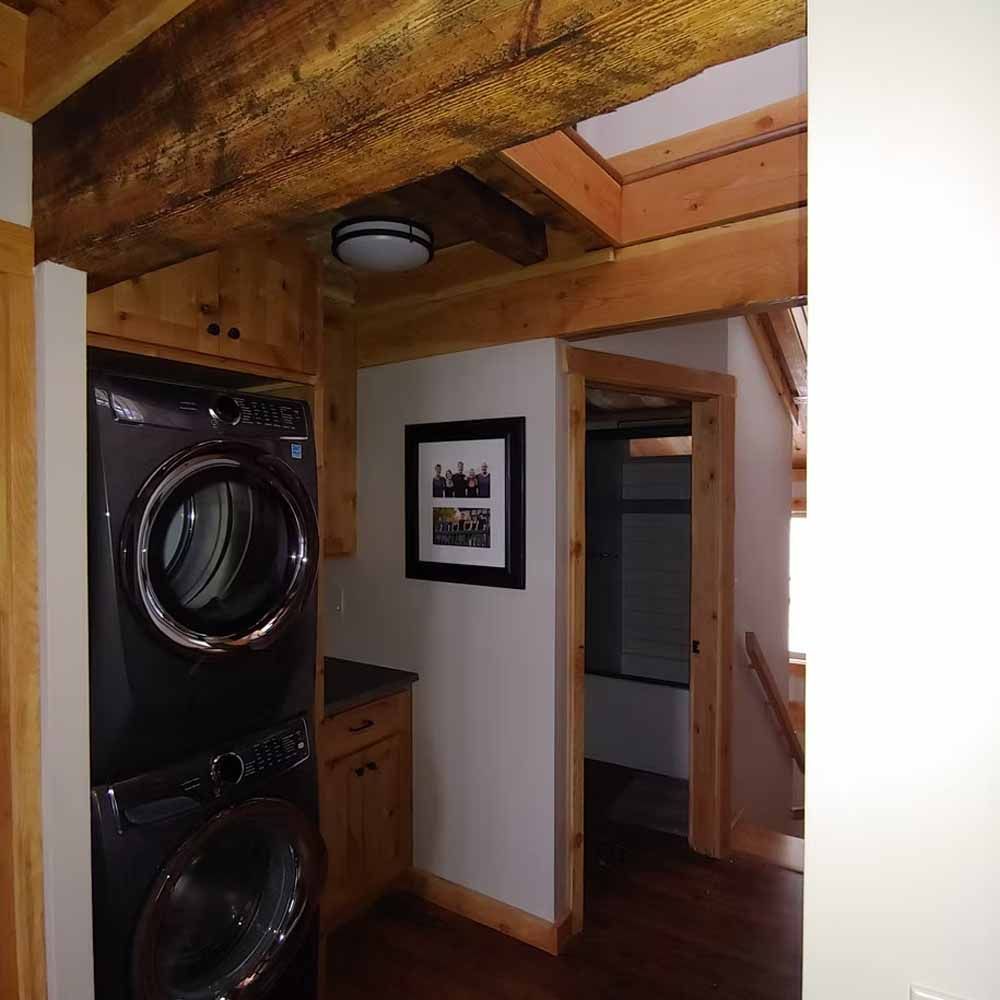 Compact laundry room with stacked black washer and dryer beneath exposed wooden beams