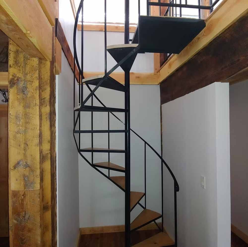 Spiral metal staircase in a narrow interior hallway with wood beams and white walls