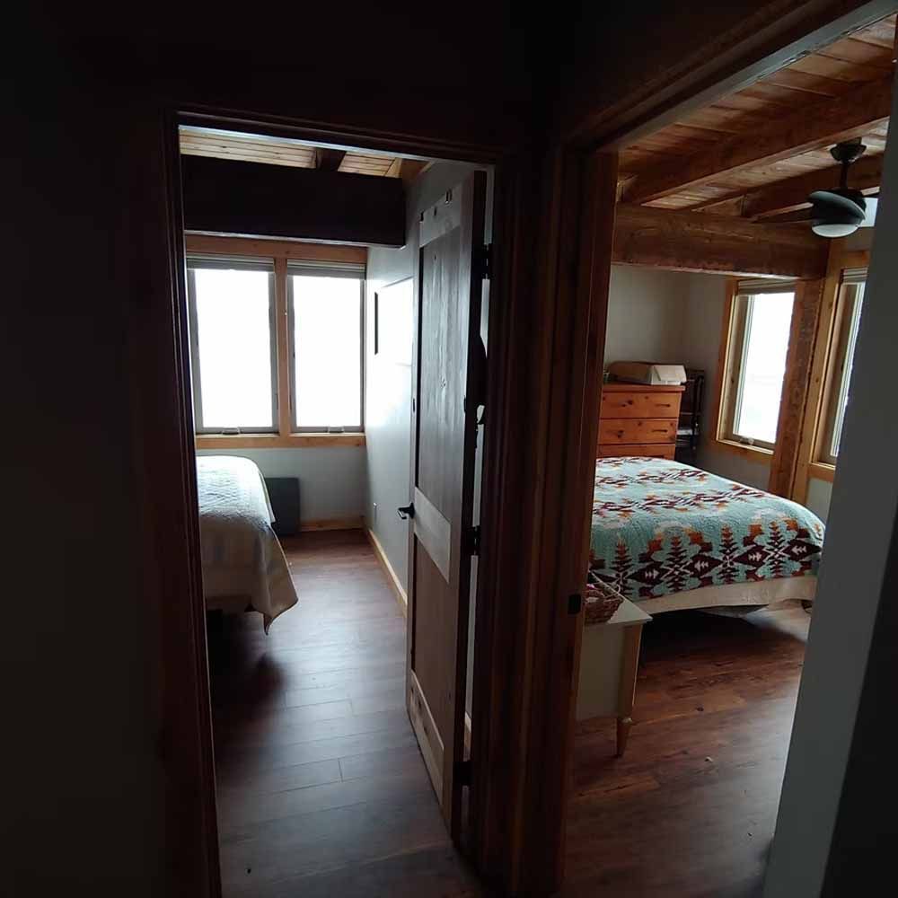 Wooden hallway view into two cozy bedrooms with windows and patterned bedding