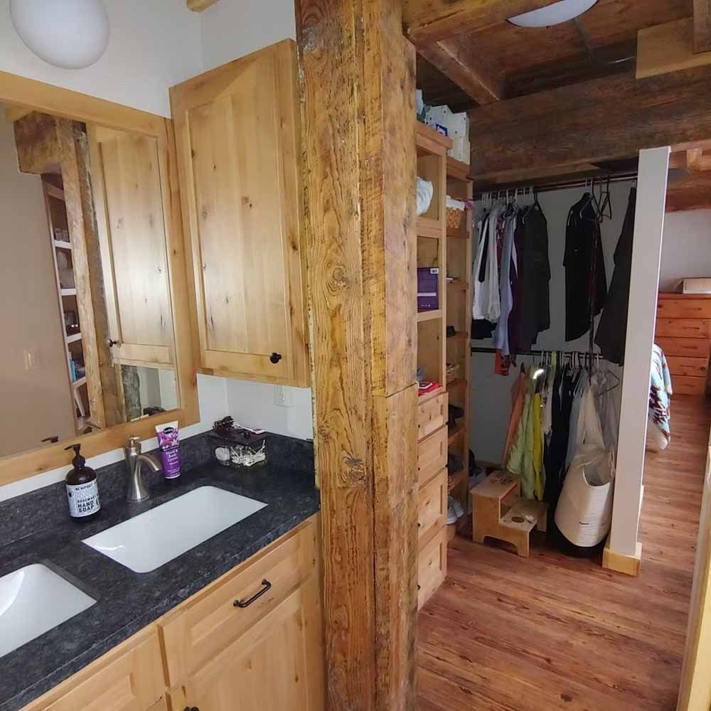 Small bathroom with wood cabinets, black countertop, mirror, and open closet beyond.