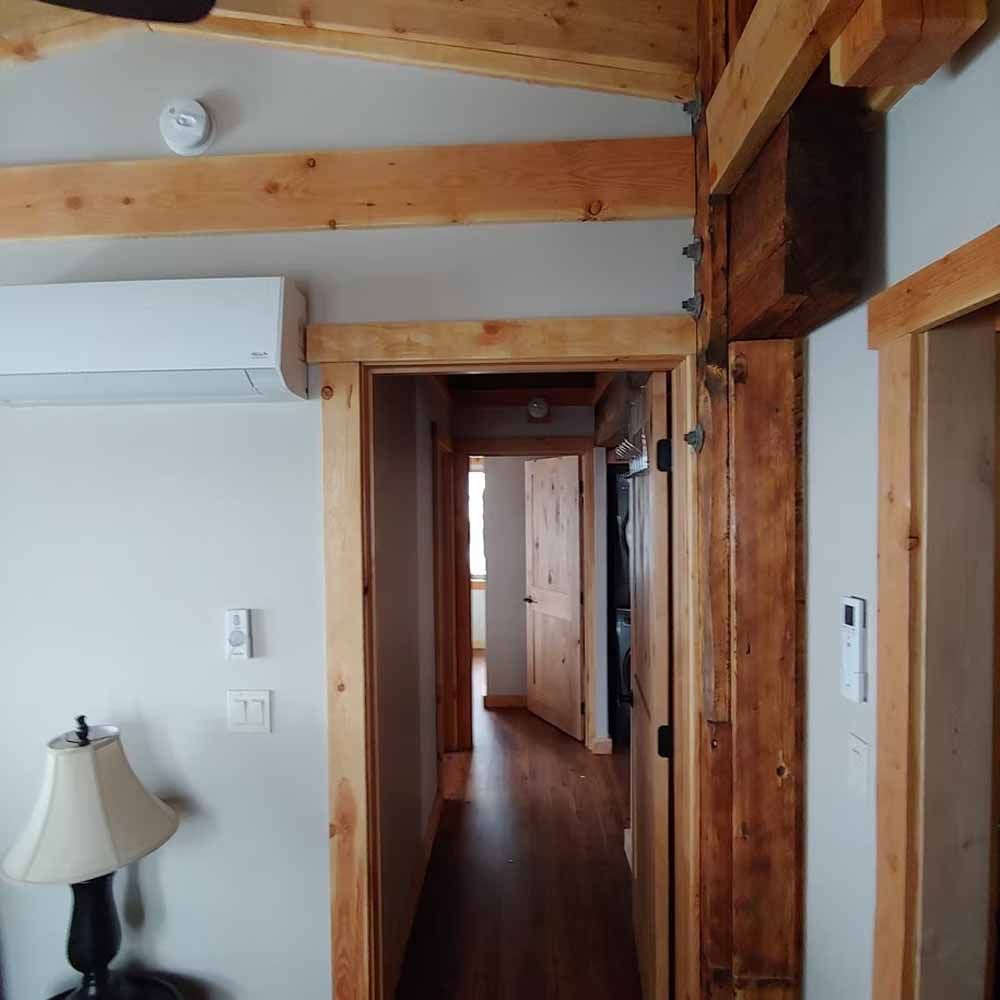 Narrow hallway with wood beams, white walls, and dark wood floors leading to another room
