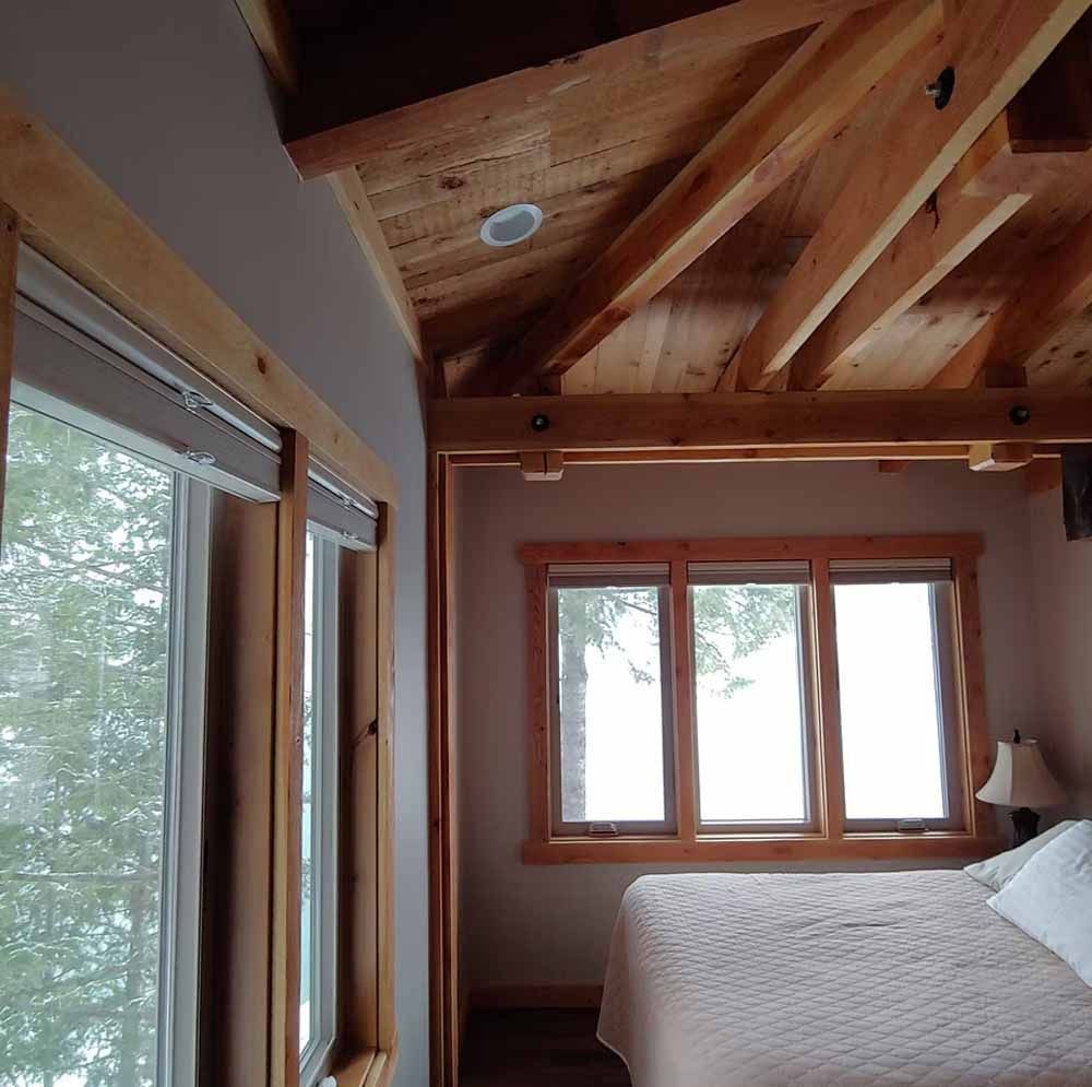 Cozy bedroom with wood-beamed ceiling, large windows, and a bed beside a floor lamp.