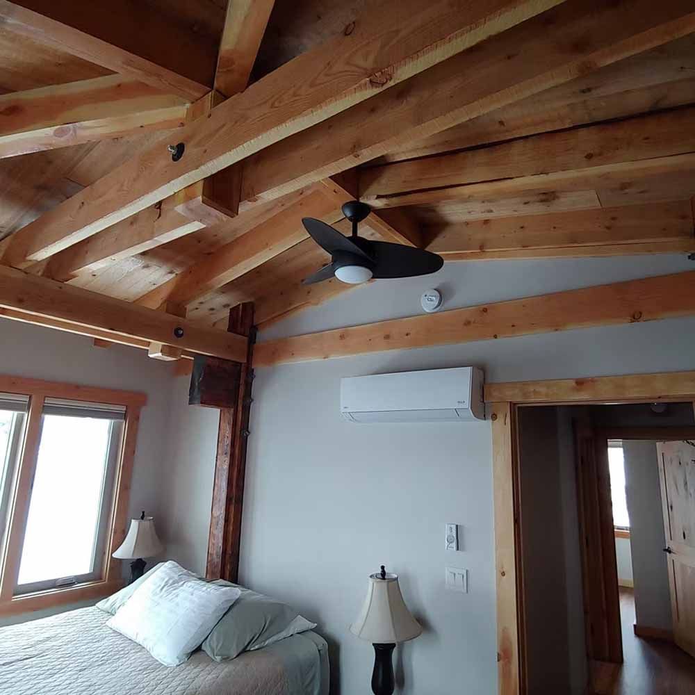 Wooden-beam bedroom with a bed, lamps, ceiling fan, and window light