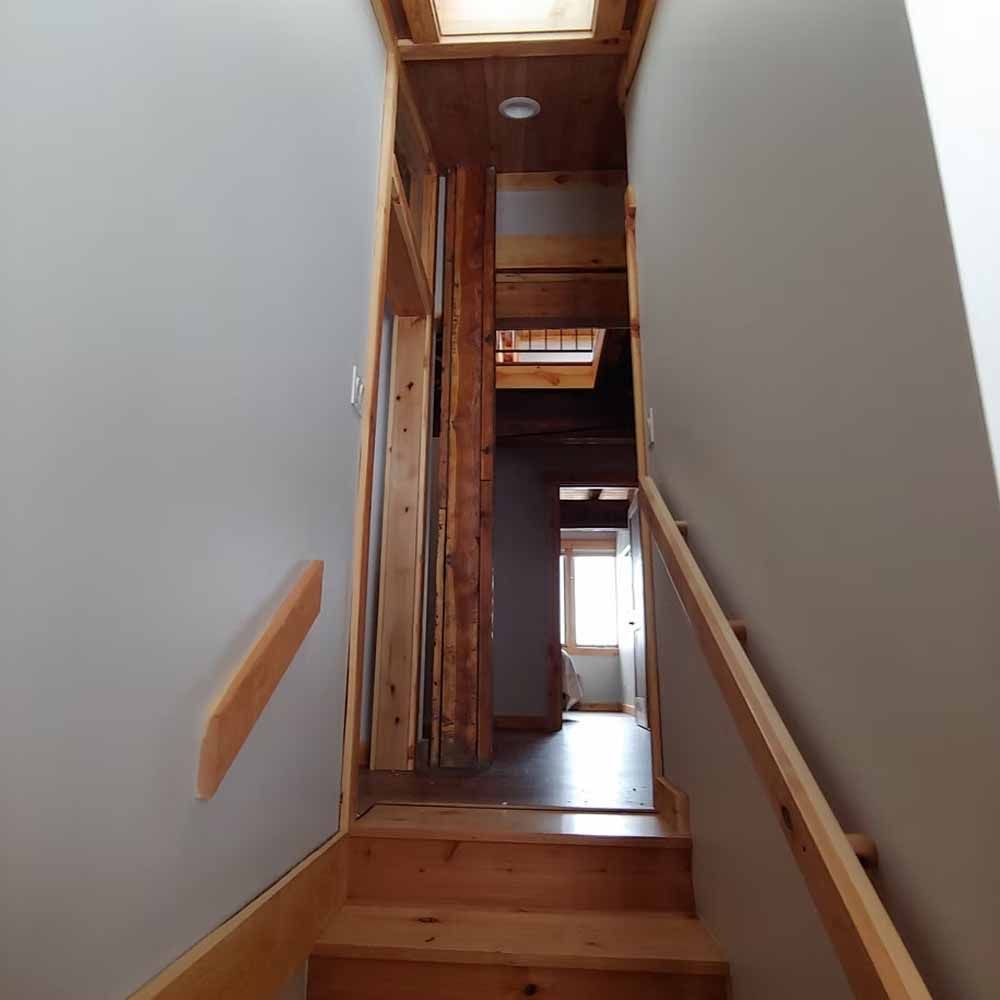 Narrow wooden stairwell leading to a hallway with skylight and doorway ahead