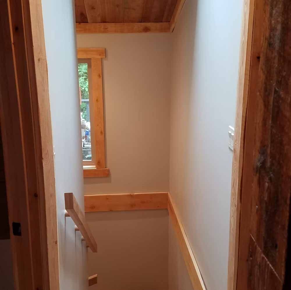 Wooden stair landing with white walls, a railing, and a window in a rustic interior