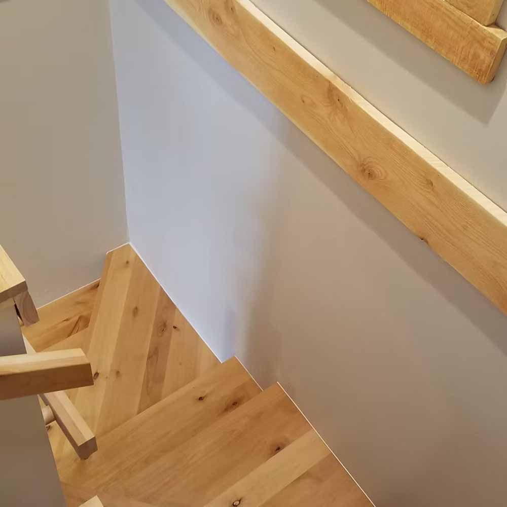 Wooden staircase with light wood handrail beside a white wall