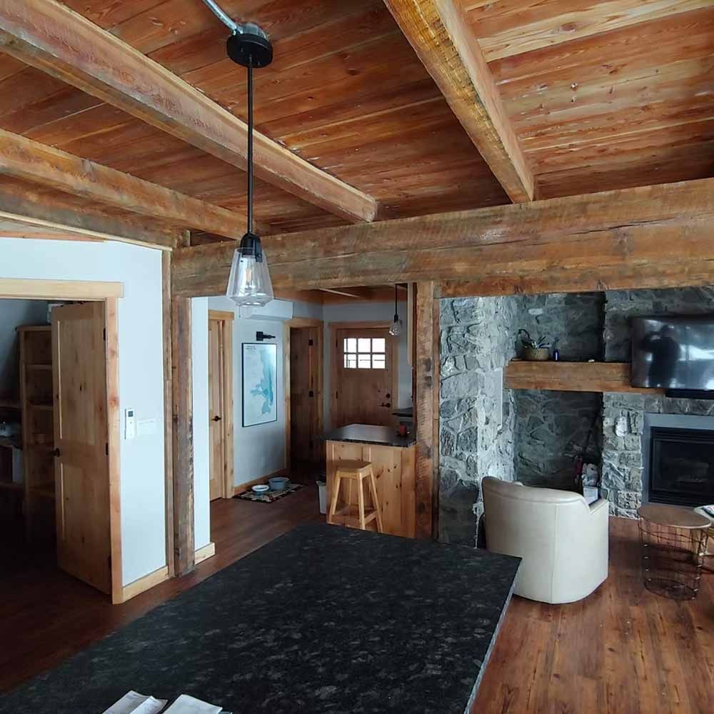 Rustic living room with wood ceiling, black rug, stone fireplace, and white chair