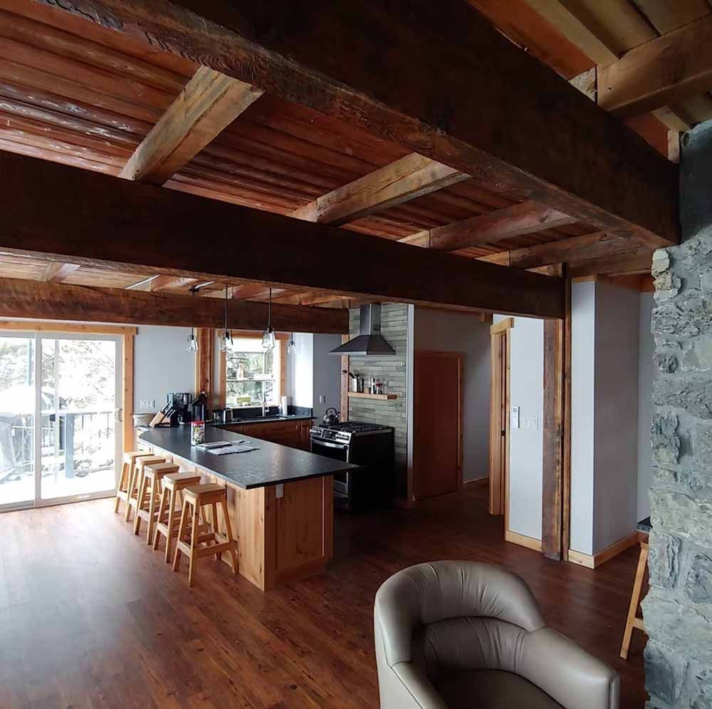 Cozy open-plan kitchen and living room with wood beams, stone fireplace, island stools, and sliding glass doors
