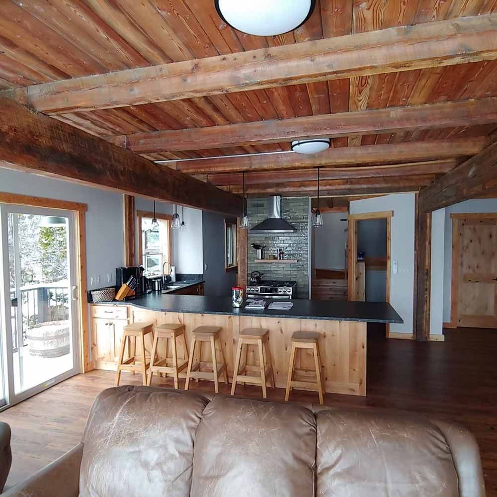 Open-plan rustic living room and kitchen with wood beams, leather sofa, and bar stools