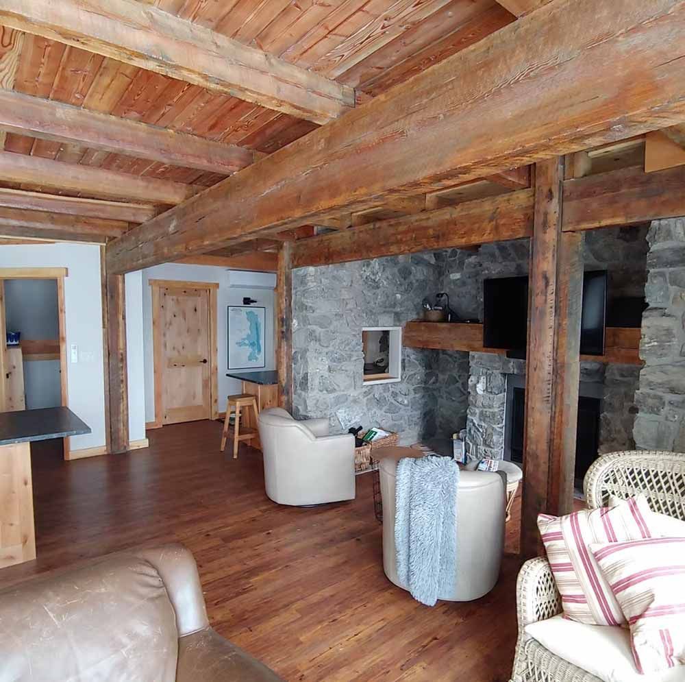 Rustic living room with exposed wood beams, stone fireplace, and leather chairs on hardwood floors.