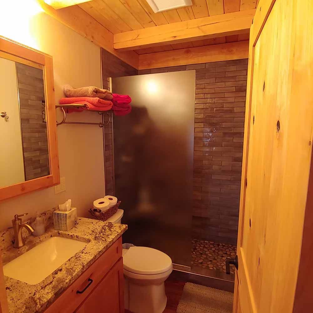Small rustic bathroom with wood walls, granite sink, toilet, and frosted glass shower.