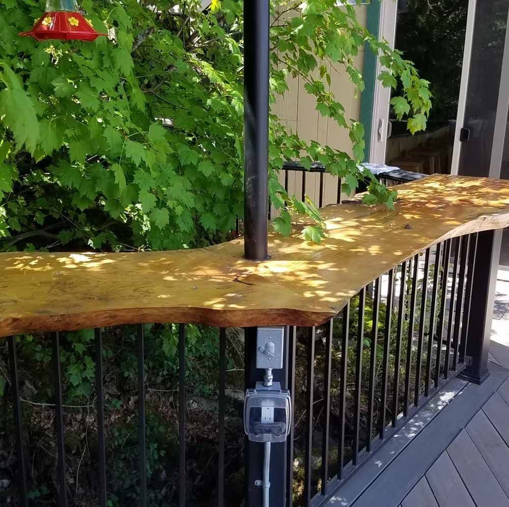Yellow-topped outdoor table beside a black railing and green foliage on a deck