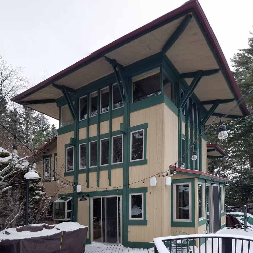 Tall modern house with green trim and a wide overhanging roof in a snowy setting