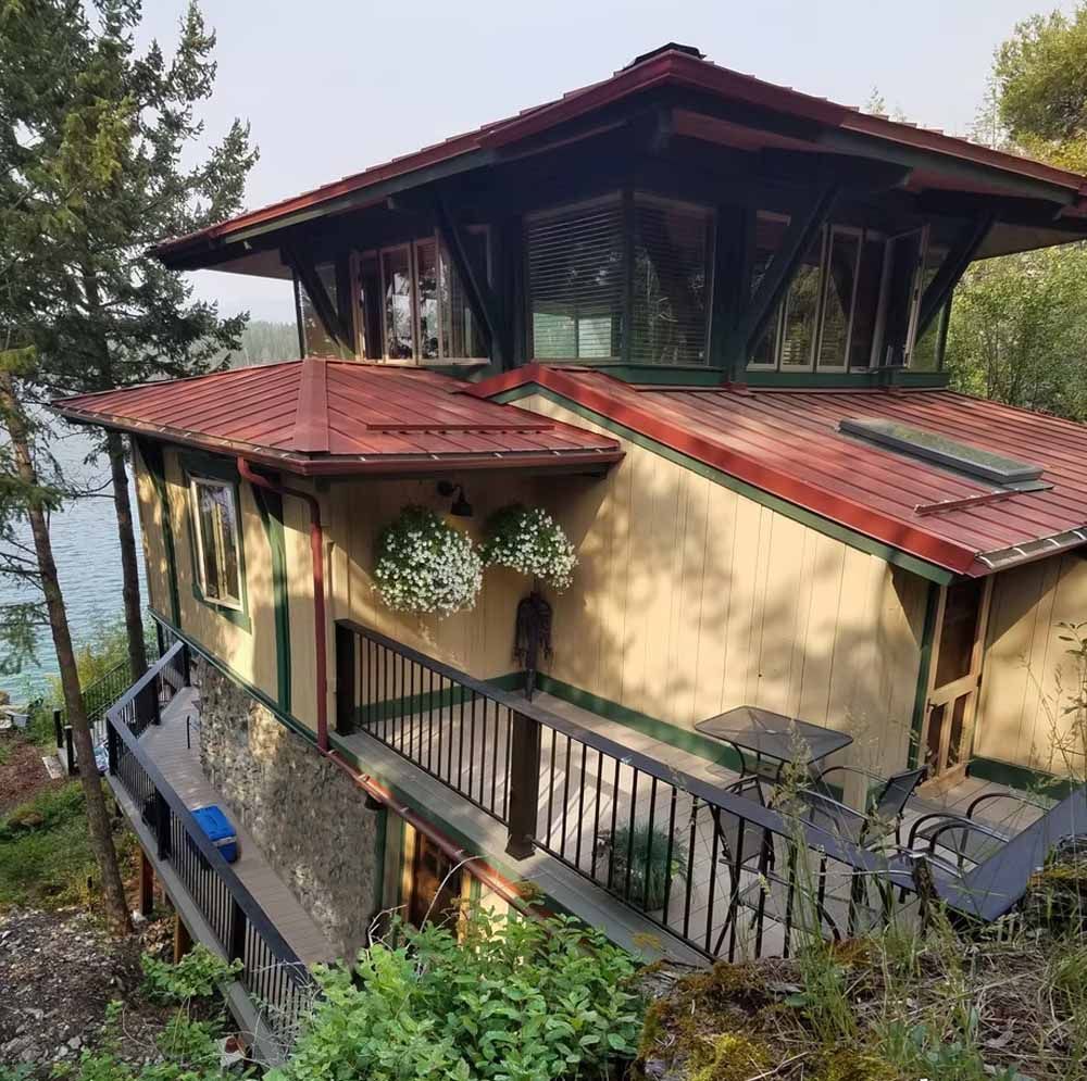 Two-story tan house with red roof and balcony, surrounded by greenery.