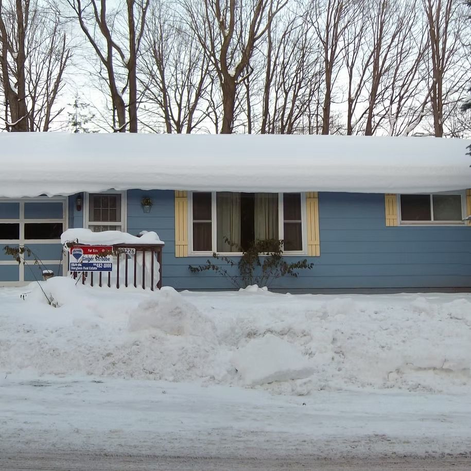 Snow-covered blue house with yellow shutters and bare trees in winter