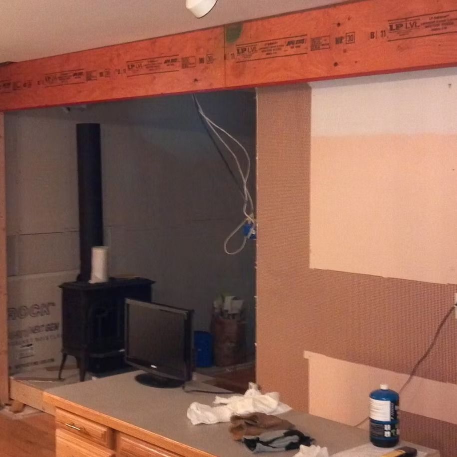 Partially finished room with exposed drywall, a small stove, TV, and construction materials on a workbench