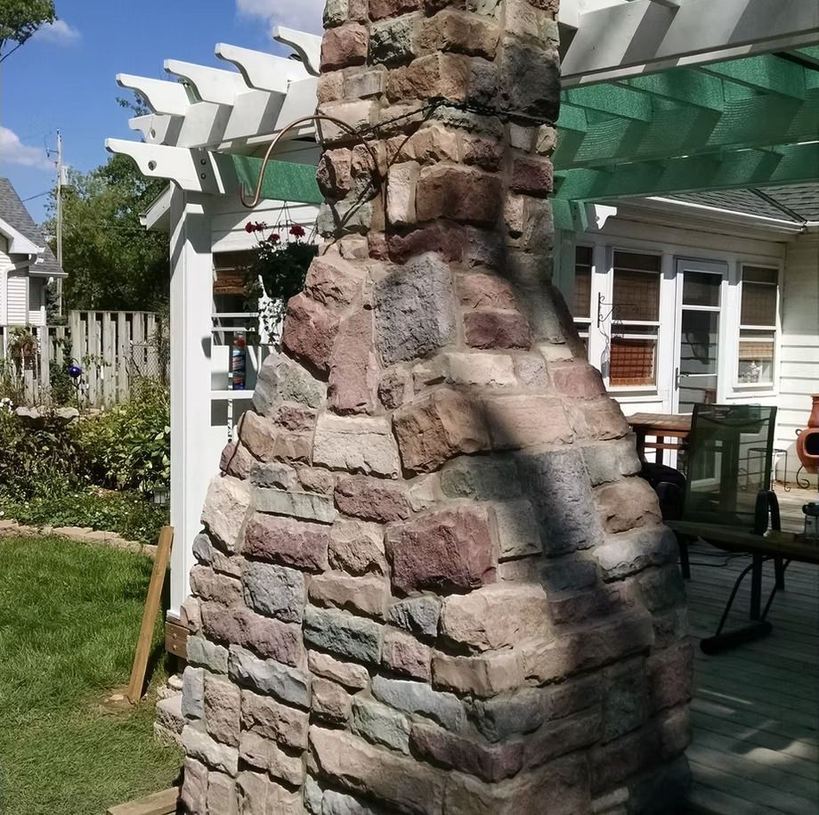 Stone outdoor fireplace under a green pergola in a backyard patio setting