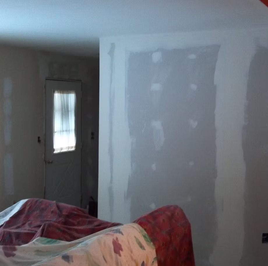 Partially painted interior wall with patchy drywall, a door, and a couch in the foreground