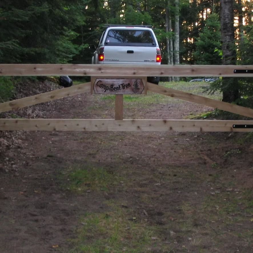 Silver SUV behind a wooden gate on a forested dirt driveway at dusk