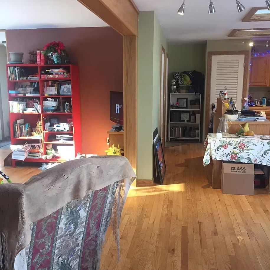 Cozy living room with red shelving, hardwood floors, and a dining area leading to a kitchen.
