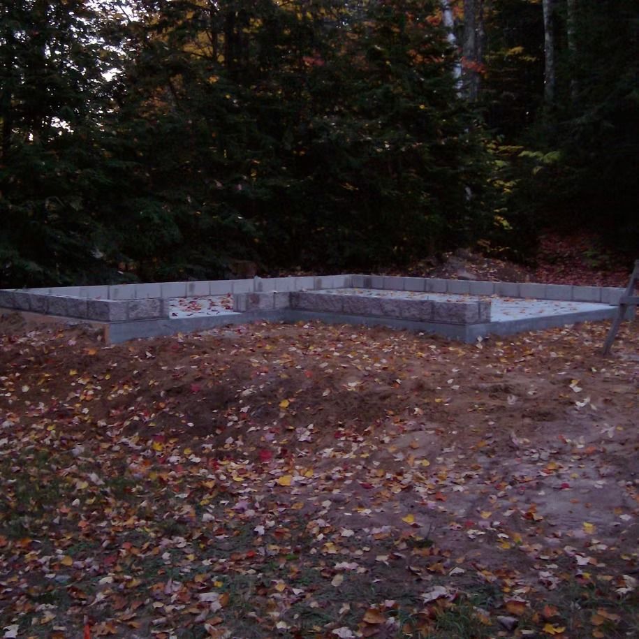 Low concrete foundation frame in a leaf-covered wooded area at dusk