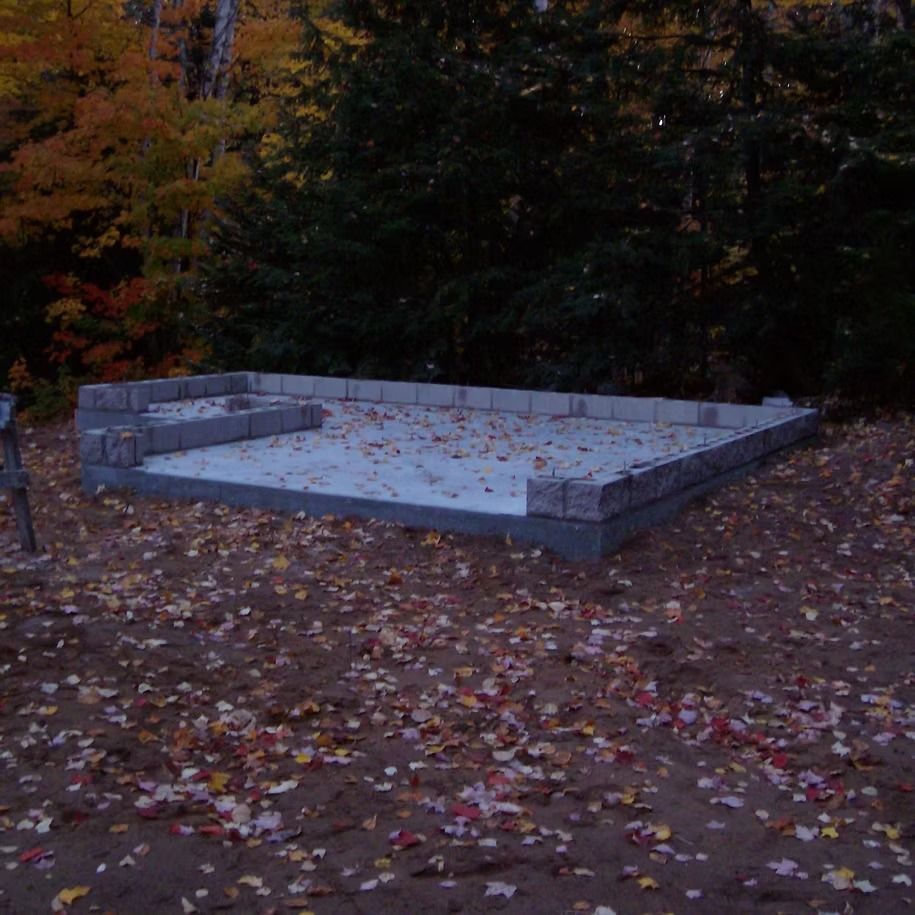 Empty concrete foundation in a wooded area with fallen autumn leaves around it