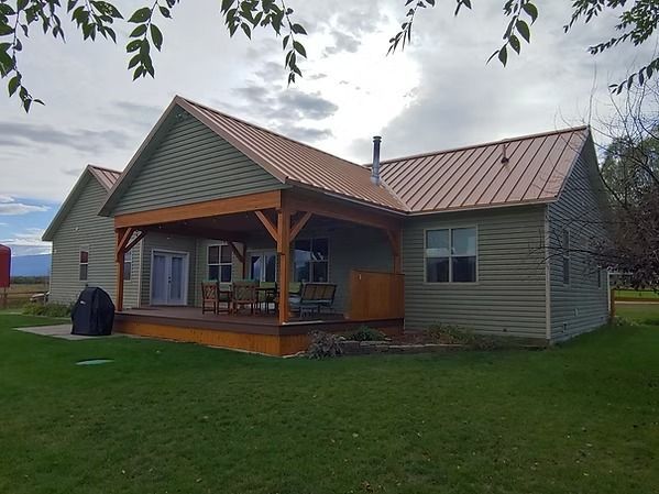 Small green house with a red roof and covered porch on a grassy lawn under cloudy skies